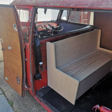Interior view of a red vehicle with a wooden bench seat and open doors.