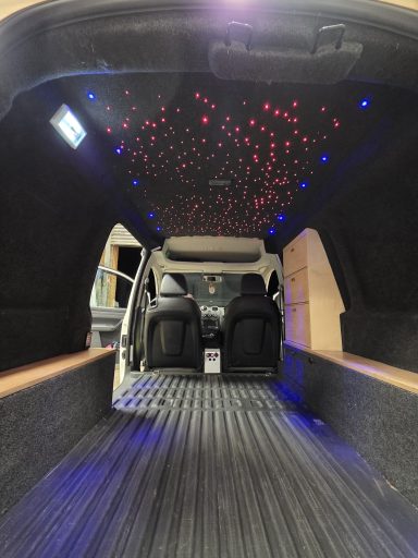 Interior of a van with a starry ceiling and dark flooring, showcasing spacious seating.