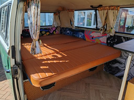 Interior of a vintage camper van with an orange foldable bed and colourful cushions.