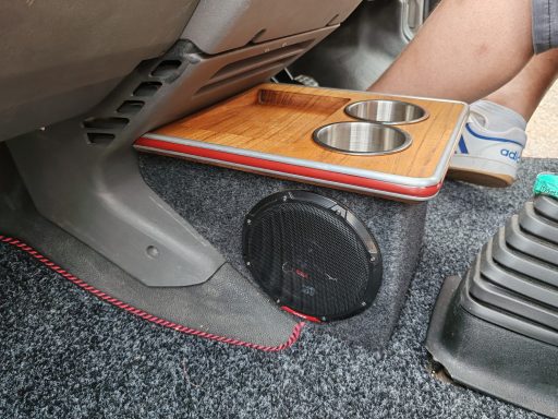 A car interior showing a custom cup holder and speaker setup near the footwell.