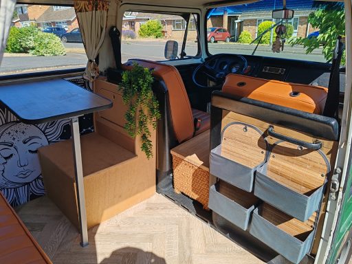 Interior of a camper van featuring seating, a table, and storage drawers.