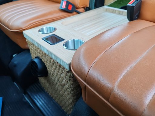 Wooden centre console with cup holders between two tan leather car seats.