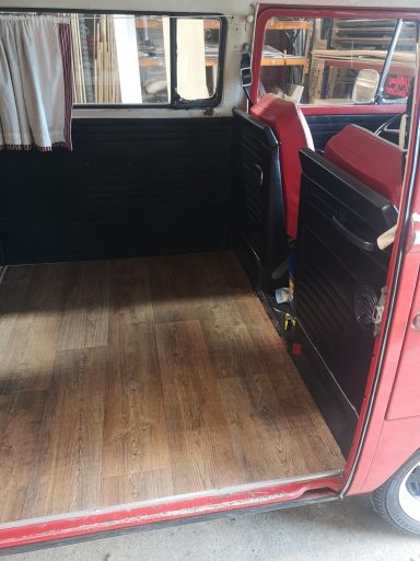 Interior of a vintage vehicle with red seating and wooden floorboards.