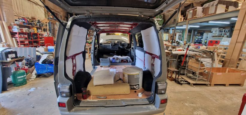 Interior of a van with open doors, showing tools and storage in a workshop setting.