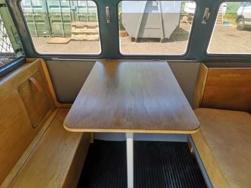 Wooden table with a white base, surrounded by bench seating in a vehicle interior.